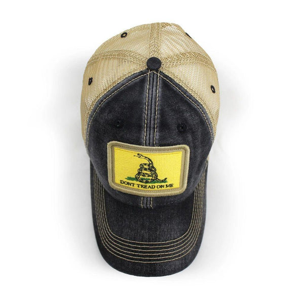 Top view of black trucker hat with khaki mesh back panels and tan stitching laying. Ballcap is embroidered with a patch of the Gadsden flag, the patch has a yellow background with a snake coiled in grass and the words Don't Tread On Me
